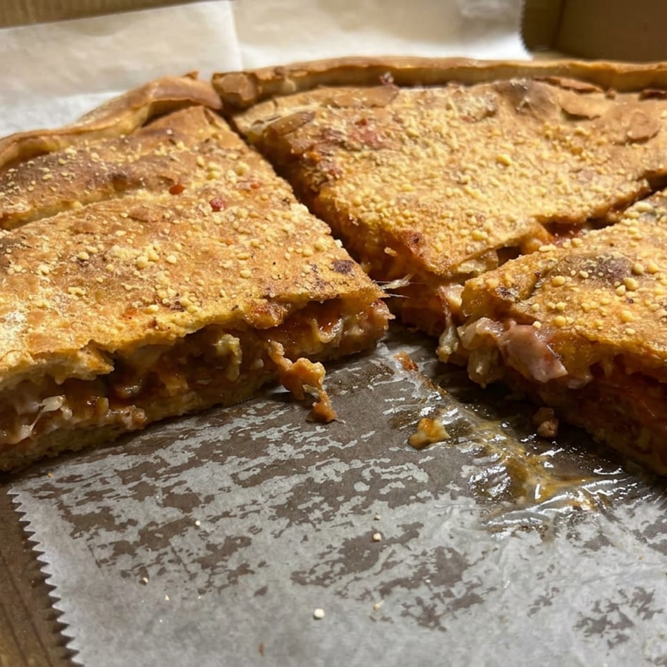 Sliced, golden-brown stuffed pizza with a sesame-studded crust sits in a cardboard box.